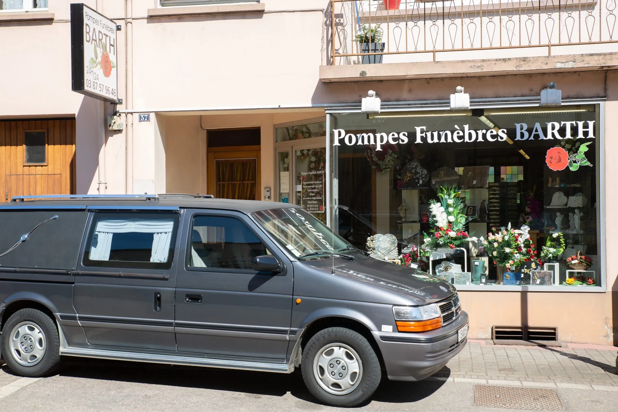 Corbillard gris stationné devant la devanture des Pompes Funèbres Barth.