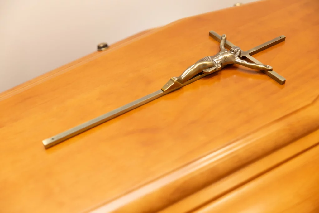 Crucifix en métal posé délicatement sur un cercueil en bois verni.